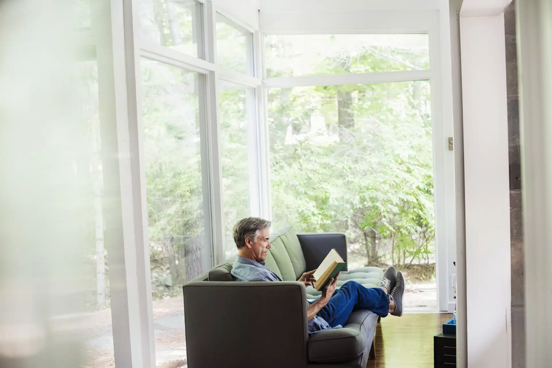 a man sitting by a window on a sofa reading a boo 2023 11 27 05 17 38 utc